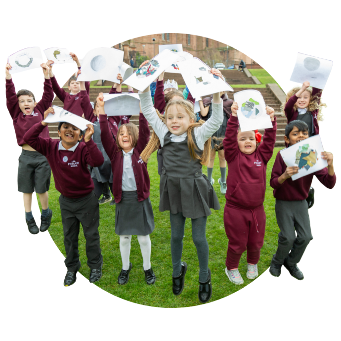 Children in school uniforms holding up drawings while standing on grass.